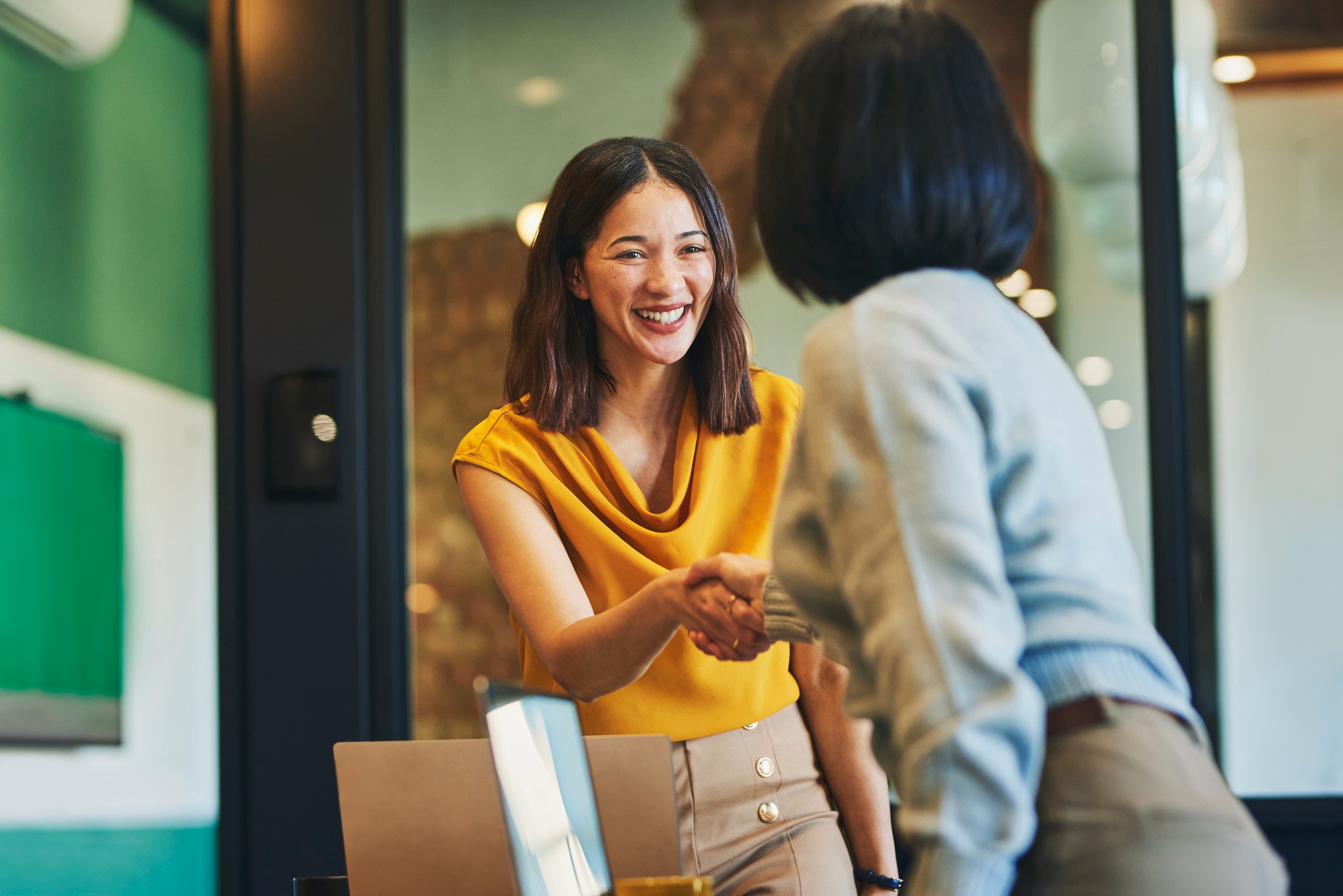 Two professional women shaking hands in an office, symbolizing financial empowerment through collaboration and support in business and finance