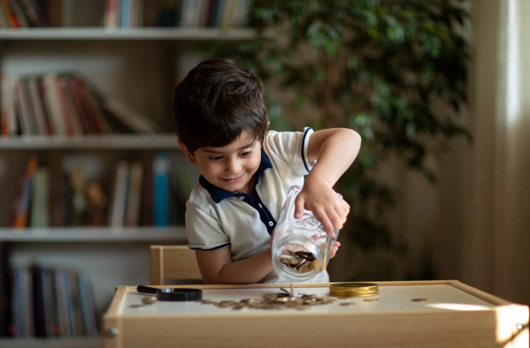 A young child learning how to save money by putting coins into a glass jar, using it as his piggy bank
