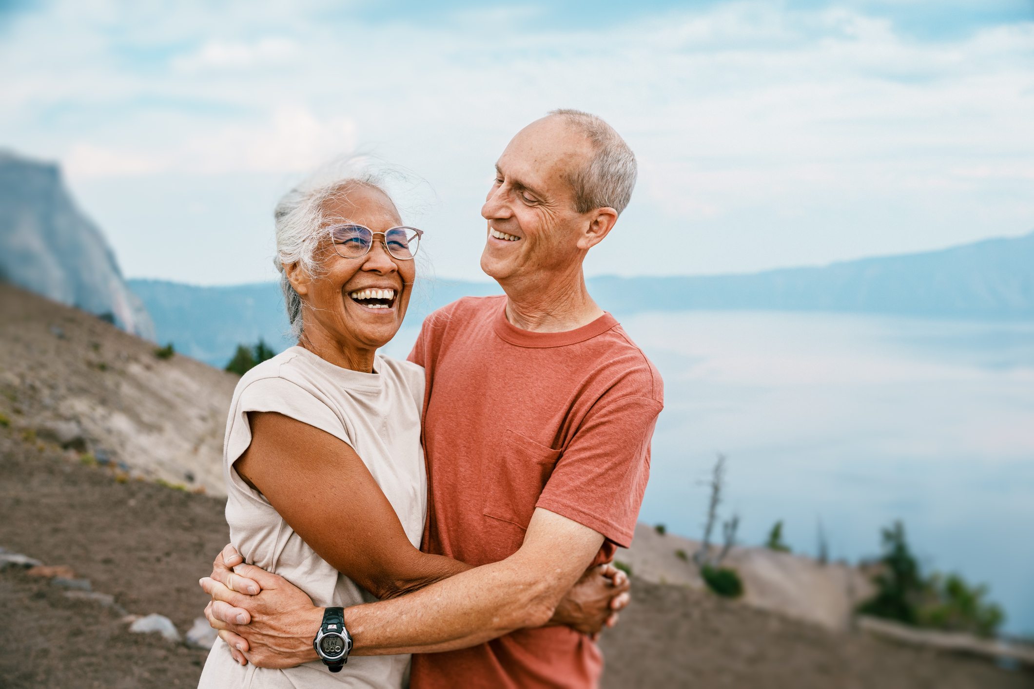 Happy retired couple embracing outdoors with scenic mountain and lake view in the background
